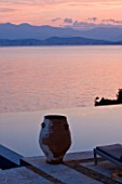 CORFU, GREECE - THE KASSIOPIA ESTATE: EVENING LIGHT - VIEW OUT TO SEA AT DUSK WITH STONE URN AND ALBANIAN MOUNTAINS IN THE DISTANCE.