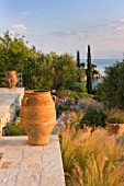 CORFU, GREECE - THE KASSIOPIA ESTATE: THE STONE TERRACE LOOKING OUT TO SEA WITH GARDEN, TERRACOTTA URNS AND OLIVE AND CYPRESS TREES