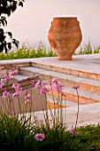 CORFU, GREECE - THE KASSIOPIA ESTATE: TERRACOTTA URN ON STONE TERRACE WITH PINK FLOWERS OF TULBAGHIA VIOLACEA