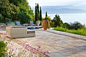 CORFU, GREECE - THE KASSIOPIA ESTATE: VIEW OUT TO SEA WITH STONE TERRACE, SEATING AREA AND TERRACOTTA URN