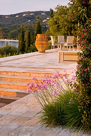 CORFU_GREECE__THE_KASSIOPIA_ESTATE_STONE_TERRACE_WITH_SEATING_AREA_HUGE_STONE_URN_AND_PINK_FLOWERS_O