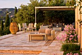CORFU, GREECE - THE KASSIOPIA ESTATE: STONE TERRACE WITH SEATING AREA, HUGE STONE URN AND PINK FLOWERS OF TULBAGHIA VIOLACEA