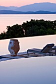 CORFU, GREECE - THE KASSIOPIA ESTATE. VIEW OF POOL TERRACE LOOKING OUT TO SEA AT DUSK WITH TERRACOTTA URN AND SUN LOUNGER. IN THE DISTANCE ARE THE ALBANIAN MOUNTAINS