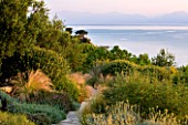CORFU, GREECE - THE KASSIOPIA ESTATE. VIEW OF GARDEN LOOKING OUT TO SEA FROM THE VILLA WITH STONE PATH AND STIPA TENUISSIMA