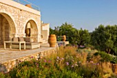 CORFU, GREECE - THE KASSIOPIA ESTATE. THE TERRACE WITH SUN LOUNGERS, TERRACOTTA URNS AND PLANTING BY JENNIFER GAY.