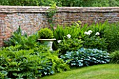 BIRTSMORTON COURT, WORCESTERSHIRE: THE END OF THE LONG BORDER WITH METAL URN PLANTED WITH BOX.  PEONY KELWAYS GLORIOUS AND  HOSTAS. WALL, WALLED GARDEN, SUMMER, GREEN, JUNE