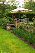 ROCKCLIFFE HOUSE, GLOUCESTERSHIRE: BORDER BESIDE WALL, STEPS AND TERRACE WITH TABLE, CHAIRS AND PARASOL - SUMMER, COUNTRY GARDEN, LAWN