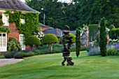 POULTON HOUSE GARDEN, WILTSHIRE: HOUSE AND LAWN WITH WITH ABSTRACT BRONZE SCULPTURE CHAIN OF EVENTS BY TONY CRAGG - IRISH YEWS - COUNTRY GARDEN, SUMMER, GREEN