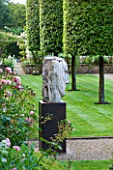 POULTON HOUSE GARDEN, WILTSHIRE: GRAVEL PATH LEADS AROUND THE EDGE OF THE WALLED GARDEN WITH CLIPPED QUERCUS ILEX TREES - MARBLE SCULPTURE - HERACLITUS - BY EMILY YOUNG