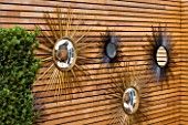 BEN DE LISI HOUSE AND GARDEN  LONDON: FRENCH SIXTIES SUNBURST MIRRORS ON WALL IN THE GARDEN
