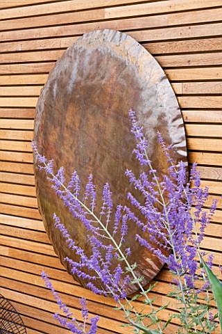 BEN_DE_LISI_HOUSE_AND_GARDEN__LONDON_COPPER_HAMMERED_DISC_ON_WALL_IN_GARDEN_WITH_PEROVSKIA
