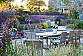 LE HAUT, GUERNSEY: VIEW ACROSS PATIO WITH LAVENDER, VERBENA BONARIENSIS, WOODEN TABLE AND CHAIRS - OUTDOOR DINING. PURPLE PLANTING SCHEME.