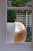 PRIVATE GARDEN LONDON: DESIGNER STEPHEN WOODHAMS - TOWN GARDEN - BASEMENT - VIEW OUT OF CONSERVATORY WINDOW TO CONTAINER WITH BOX BALL, SCULPTURE POMME BY CLAUDE LALANNE, TRELLIS
