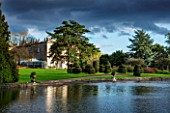 THORP PERROW ARBORETUM, YORKSHIRE - VIEW ACROSS THE LAKE TO THE HOUSE IN AUTUMN. CLASSIC COUNTRY GARDEN, STORMY, WATER