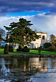 THORP PERROW ARBORETUM, YORKSHIRE - VIEW ACROSS THE LAKE TO THE HOUSE IN AUTUMN. CLASSIC COUNTRY GARDEN, STORMY, WATER
