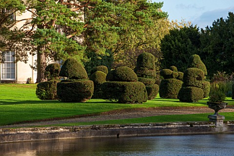 THORP_PERROW_ARBORETUM_YORKSHIRE_VIEW_ACROSS_LAKE_IN_AUTUMN_TO_LAWN_AND_CLIPPED_TOPIARY_YEW__FORMAL_