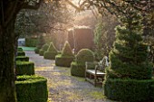 HOLKER HALL  CUMBRIA: EARLY MORNING LIGHT ON TOPIARY AND A WOODEN SEAT IN THE FORMAL GARDEN