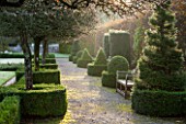 HOLKER HALL  CUMBRIA: EARLY MORNING LIGHT ON TOPIARY AND A WOODEN SEAT IN THE FORMAL GARDEN