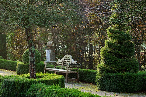 HOLKER_HALL__CUMBRIA_EARLY_MORNING_LIGHT_ON_TOPIARY_AND_A_WOODEN_SEAT_IN_THE_FORMAL_GARDEN