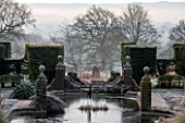 SEDGWICK PARK, WEST SUSSEX. COLUMNS OF YEW FLANK BESIDE THE LONG CANAL ALSO KNOWN AS THE WHITE SEA WITH PAMPAS GRASS. WINTER, GARDEN, FROST, JANUARY, WATER, FORMAL