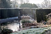 SEDGWICK PARK, WEST SUSSEX. COLUMNS OF YEW BESIDE THE LONG CANAL ALSO KNOWN AS THE WHITE SEA WITH PAMPAS GRASS. WINTER, GARDEN, FROST, JANUARY, WATER.