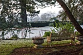 SEDGWICK PARK, WEST SUSSEX. ORNATE METAL BENCH WITH STONE URNS. VIEW OUT TOWARDS FORMAL GARDEN WITH CLIPPED YEW HEDGING. WINTER, JANUARY