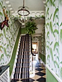 BUTTER WAKEFIELD HOUSE, LONDON. THE HALLWAY. CHRISTMAS: STRIKING ENTRANCE WITH PALM FROND DECORATED WALLPAPER AND STRIPED CARPET ON STAIRS