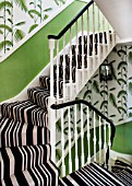 BUTTER WAKEFIELD HOUSE, LONDON. THE HALLWAY AND STAIRS AT CHRISTMAS. DETAIL OF BOLD STRIPED STAIR CARPET AND PALM FROND WALLPAPER UP TO LANDING