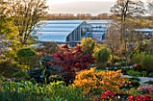 RHS GARDEN, WISLEY, SURREY: SPRING - VIEW FROM TOP OF ROCK GARDEN TO THE GLASSHOUSE - EVENING LIGHT
