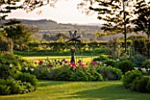 THE OLD VICARAGE, WORMLEIGHTON, WARWICKSHIRE: DESIGNER ANGEL COLLINS - SUNDIAL BED WITH TULIPS BESIDE LAWN WITH VIEW TO COTSWOLDS BEYOND - CLASSIC COUNTRY GARDEN