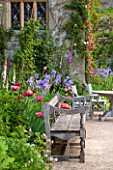 HADDON HALL, DERBYSHIRE: TERRACE BESIDE HALL WITH WOODEN BENCH, TABLE AND CHAIRS, ROSES, POPPIES AND IRISES