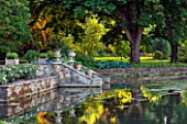 ABLINGTON MANOR  GLOUCESTERSHIRE: VIEW ACROSS COLN RIVER TO STONE STEPS AND CONTAINERS WITH REFLECTIONS OF TREES IN WATER. CLASSIC COUNTRY GARDEN  COTSWOLDS  ROMANTIC  ROMANCE