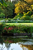 ABLINGTON MANOR  GLOUCESTERSHIRE: VIEW ACROSS COLN RIVER TO ISLAND BED AND CLIPPED YEW TOPIARY. REFLECTIONS  WATER. CLASSIC COUNTRY GARDEN  COTSWOLDS  ROMANTIC  ROMANCE  LAWN