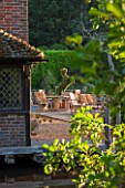 OLD NETLEY MILL, SHERE, SURREY: DECKED TERRACE WITH TABLE AND CHAIRS BESIDE THE LAKE AND TOPIARY HORSE IN CONTAINER. JUNE, SUMMER