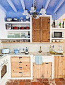 CIUTADELLA MENORCA, SPAIN: EVELYNE MANDEL HOUSE - BLUE AND WHITE KITCHEN - STONE SINK, BLUE SMEG TOASTER, MICROWAVE AND WOODEN CUPBOARDS. TERRACOTTA TILES ON FLOOR