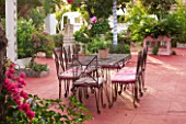 JONATHAN BAILLIE GARDEN, ALAIOR, MENORCA: PATIO WITH RED FLOOR, METAL TABLE AND CHAIRS, BOUGAINVILLEA, TREE PAINTED WITH WHITE AND BLUE STRIPES. MEDITERRANEAN, DINING, RELAXING
