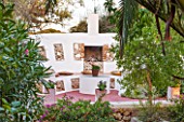 JONATHAN BAILLIE GARDEN, ALAIOR, MENORCA: WHITE WASHED WALL WITH SEATING AND FIREPLACE AND CUSHIONS, SEATING, A PLACE TO SIT, FIRE PLACE, ENTERTAINING, OUTDOOR LIVING