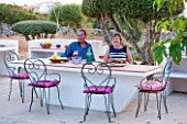 JONATHAN BAILLIE GARDEN, ALAIOR, MENORCA: JONATHAN AND JO BAILLIE AT THE OUTDOOR BUILT IN TABLE AND BARBEQUE. OUTDOOR LIVING, ENTERTAINING
