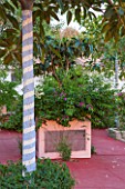 JONATHAN BAILLIE GARDEN, ALAIOR, MENORCA: PATIO WITH RED FLOOR, RAISED BED WITH TREE PAINTED IN BLUE AND WHITE STRIPES