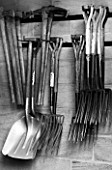 WEST DEAN GARDENS, WEST SUSSEX: BLACK AND WHITE IMAGE OF GARDEN TOOLS HANGING UP IN THE WALLED KITCHEN GARDEN. AUGUST