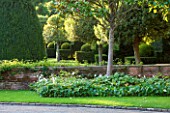 GREAT FOSTERS. SURREY: VIEW OF FRONT OF THE HOTEL WITH CLIPPED TOPIARY SHAPES IN EVENING LIGHT -  CLASSIC COUNTRY GARDEN, FORMAL