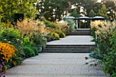 RHS GARDEN, WISLEY, SURREY: THE BOWES - LYON ROSE GARDEN WITH PLANTING OF ROSES AND STIPA GIGANTEA IN SUMMER - SEPTEMBER - EVENING LIGHT - PATH