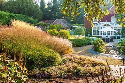 SURREY_GARDEN_DESIGNED_BY_ANTHONY_PAUL_VIEW_TO_THE_HOUSE_WITH_GRASSES_AND_CIRCULAR_POOL_WITH_PONTADE