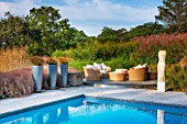 SURREY GARDEN DESIGNED BY ANTHONY PAUL: SWIMMING POOL WITH TERRACE - RATTEN FURNITURE, CUSHIONS, CAREX FLAGELLIFERA IN METAL CONTAINERS. WATER, COUNTRY GARDEN, CLASSIC