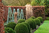 RODE HALL AND GARDENS, CHESHIRE: BORDER WITH BEECH HEDGE, BLUE WOODEN TRIPODS, GRASSES AND LAWN. COUNTRY GARDEN, GREEN, WINTER, FEBRUARY