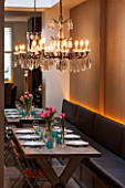 SALLY STOREY HOUSE, LONDON: DINING AREA WITH WOODEN TABLE, DINING CHAIRS, CHANDELIER AND BANQUETTE SEATING, MIRROR, TULIPS. ENTERTAINING, SEAT, SEATS, LIGHTING, LIGHTS