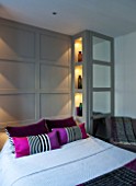 SALLY STOREY HOUSE, LONDON: BEDROOM WITH BED, PINK CUSHIONS, GREY WOODEN PANELING AND GLASS BOTTLES IN RECESSED SHELVES - SHELVING, LIGHT, LIGHTS, LIGHTING
