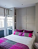 SALLY STOREY HOUSE, LONDON: BEDROOM WITH BED, PINK CUSHIONS, GREY WOODEN PANELING AND GLASS BOTTLES IN RECESSED SHELVES - SHELVING