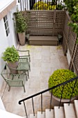 DESIGNER STEPHEN WOODHAMS, LONDON: FORMAL TOWN GARDEN IN SPRING - BASEMENT, TERRACE WITH CONTAINERS AND METAL SEATS. STEPS, STAIRS, STAIRWAY, TRELLIS, BOX, BUXUS, PAVING