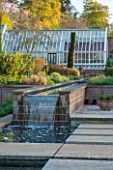 BROUGHTON GRANGE, OXFORDSHIRE: DESIGNER TOM STUART-SMITH - POOL AND WATERFALL IN THE WALLED GARDEN WITH GREENHOUSE BEHIND - SPRING, WATER, STEPPING STONES